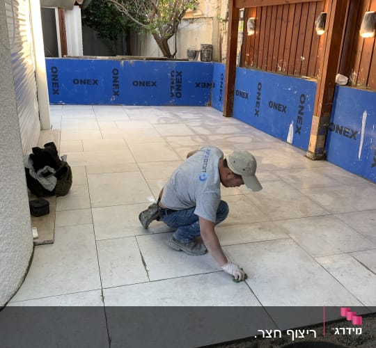 עובד מתקין אריחי רצפה בחצר עם כלים וחומרים